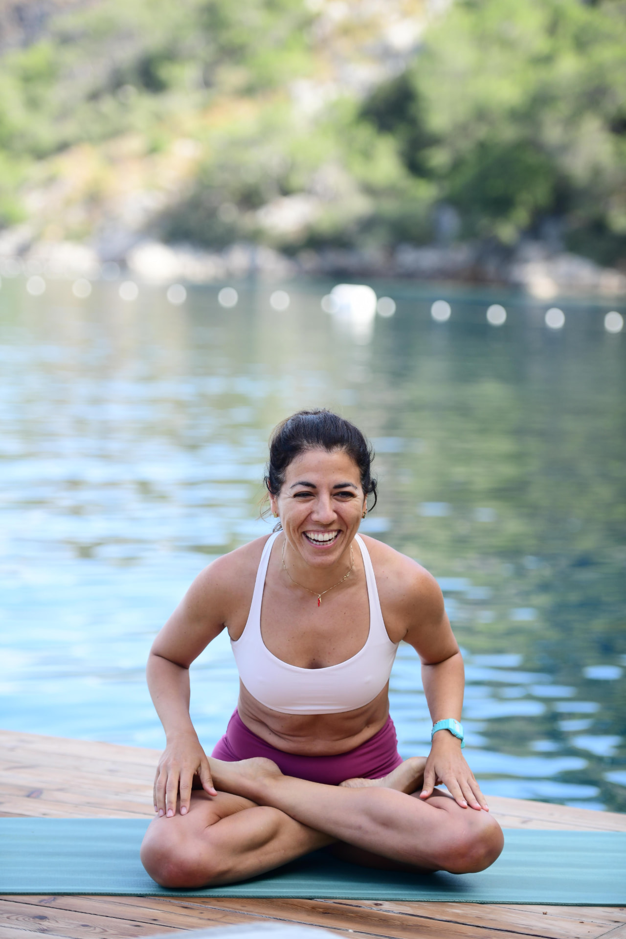 Selale smiling while seated in a yoga pose by the water