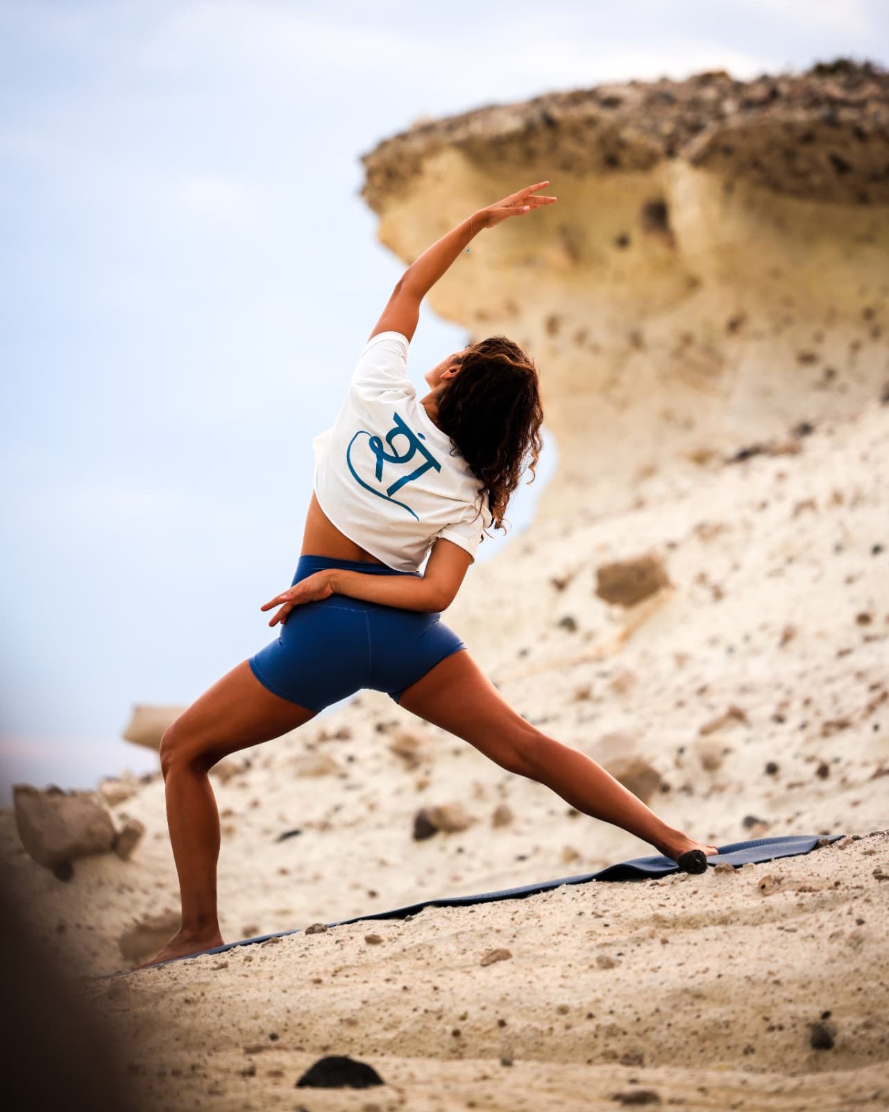 Şelale in reverse warrior pose on a mat beside a sculpted rock formation