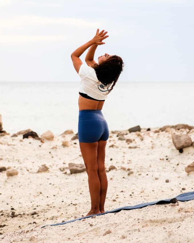 Şelale standing on a mat with hands in prayer overhead, facing the open sea
