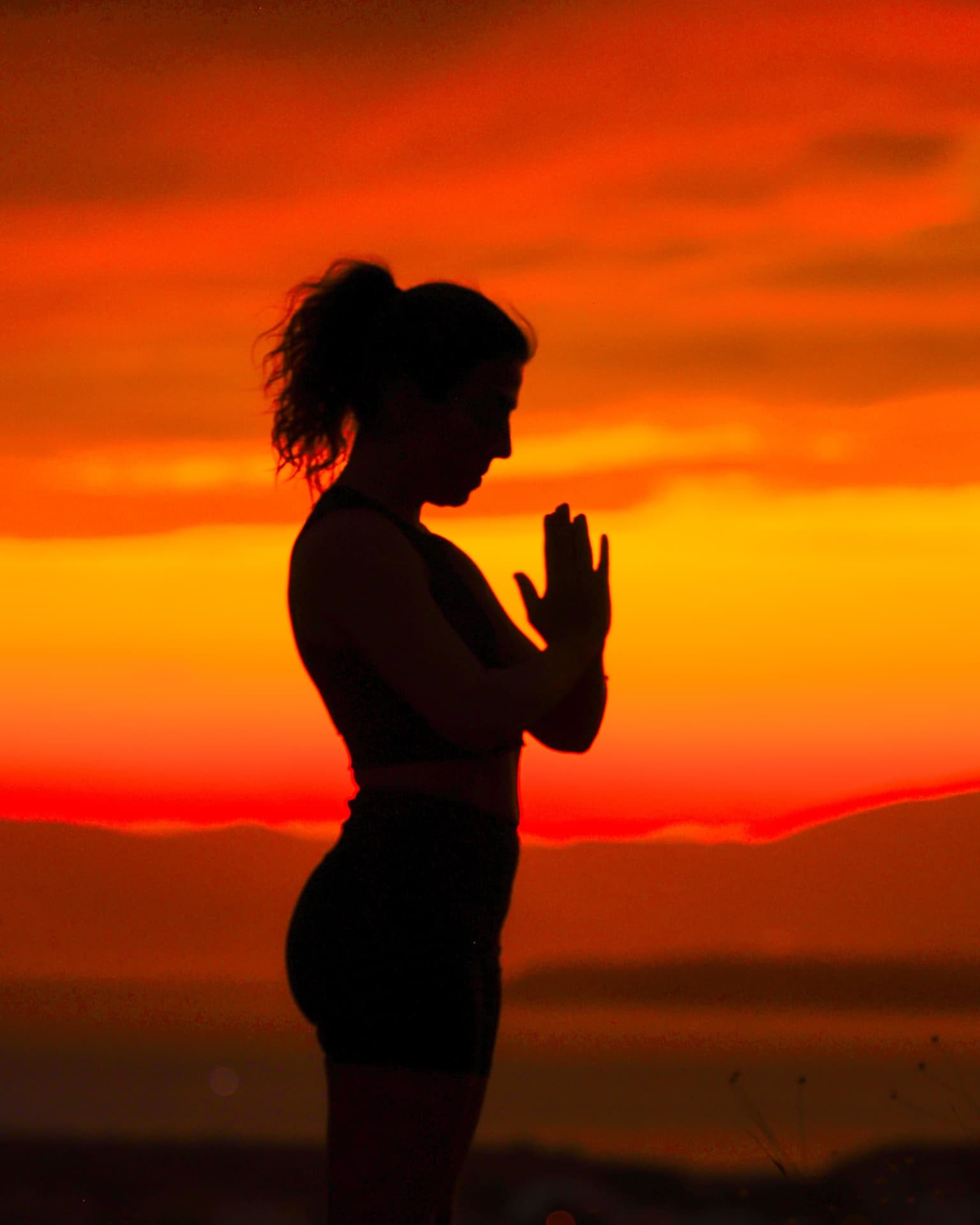 Silhouette of Şelale in prayer pose against a deep red sunset