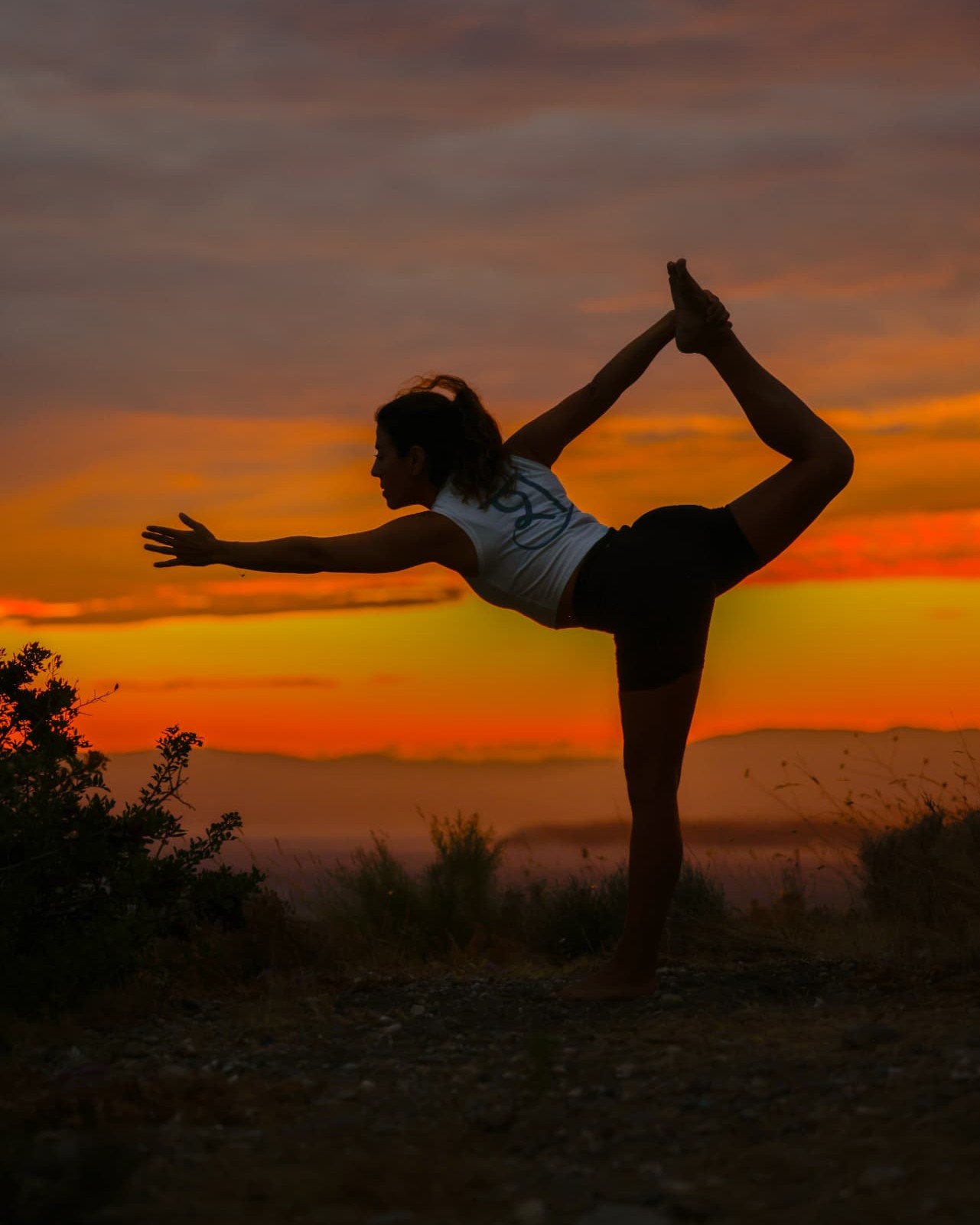 Şelale in dancer pose on a hilltop against a fiery sunset sky