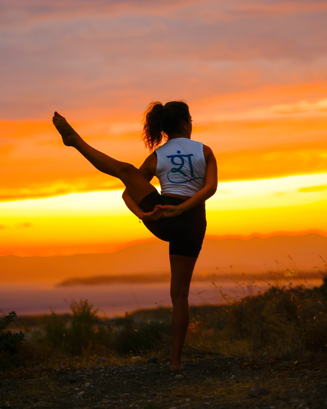 Şelale held in a standing balance pose, seen from behind against an orange dusk sky