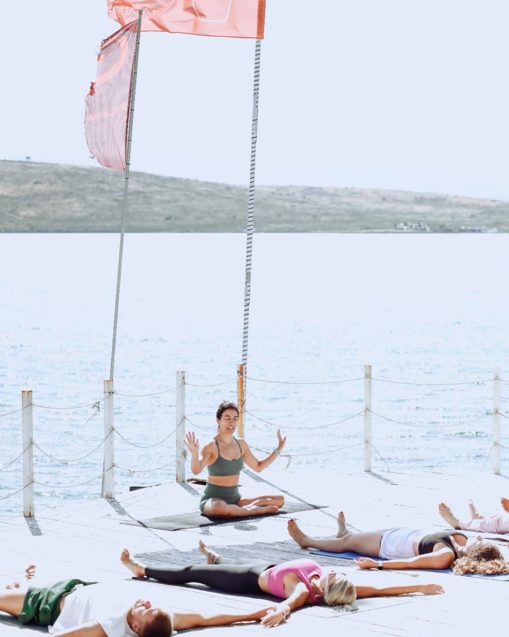 Şelale leading a seaside class while participants rest on mats across the deck